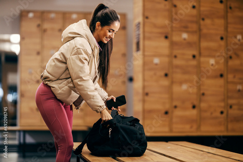 A fit sportswoman is packing sports clothes in her bag while standing in gym fitting room. photo