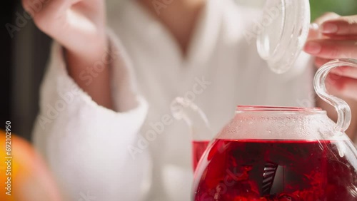 Woman stirs hibiscus tea in teapot closeup photo