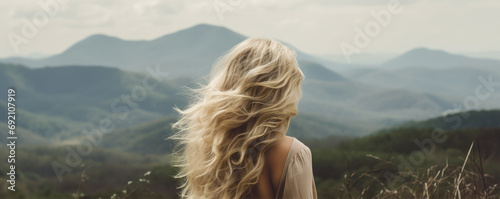 Woman with long wavy blond hairs with nature in background.  Dense long blonde hair rear view photo