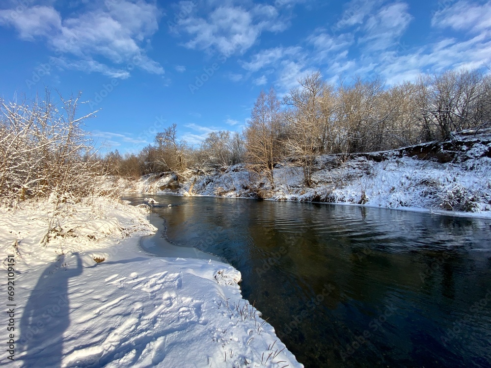 Winter landscape on the bank of the river in sunny weather, the shadow of a man falls on the snow, the quiet waters of the forest river. First snow. Winter landscape on the bank of the river in sunny weather, the shadow of a man falls on the snow, the quiet waters of the forest river. First snow.