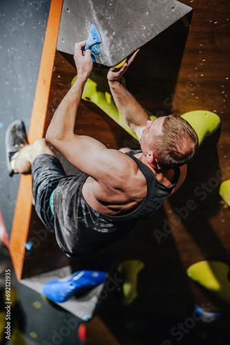 Young athletic guy in black tank top climbing climbing wall at climbing competition
