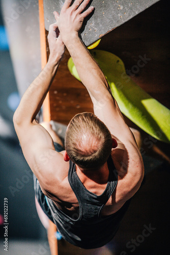 Young athletic guy in black tank top climbing climbing wall at climbing competition