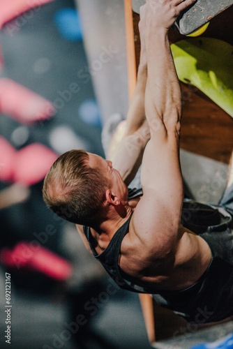 Young athletic guy in black tank top climbing climbing wall at climbing competition