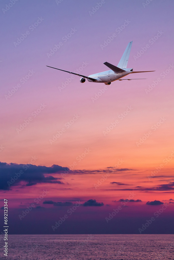 A large wide body passenger aircraft fly over the sea against the backdrop of a scenic sundown sky