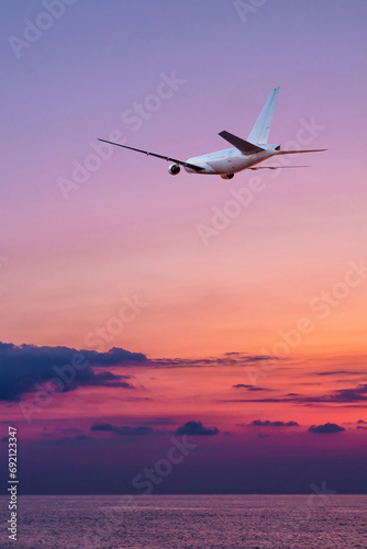 A large wide body passenger aircraft fly over the sea against the backdrop of a scenic sundown sky