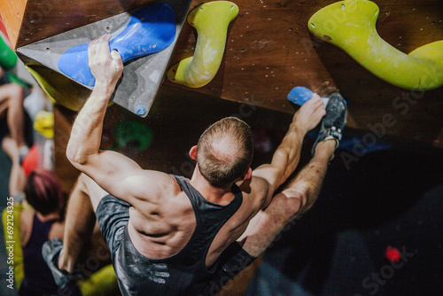 Young athletic guy in black tank top climbing climbing wall at climbing competition