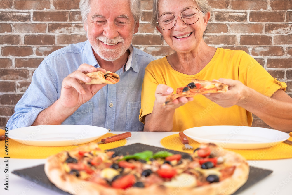 Happy senior couple ready to bite a slice of pizza. Elderly woman and man share a traditional Italian pizza for dinner Happy senior couple ready to bite a slice of pizza. Elderly woman and man share a traditional Italian pizza for dinner