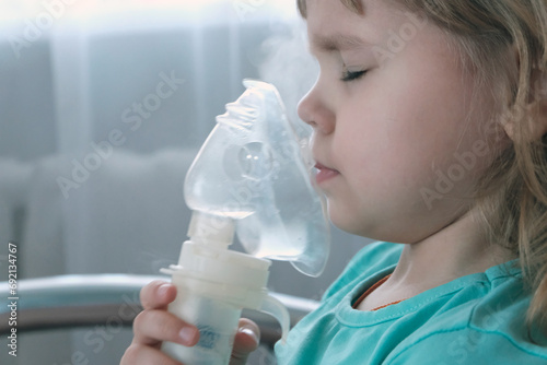 A little girl, a child of European appearance, wearing an inhaler mask. Treatment of seasonal diseases with a nebulizer at home. photo