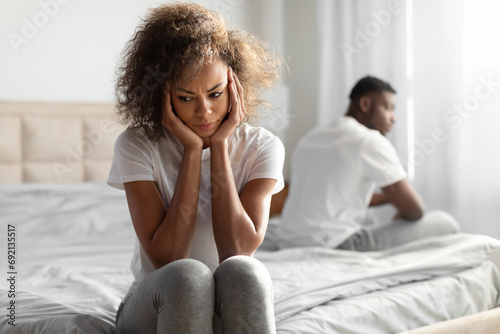 Unhappy Black Couple Sitting On Different Sides Of Bed Indoor