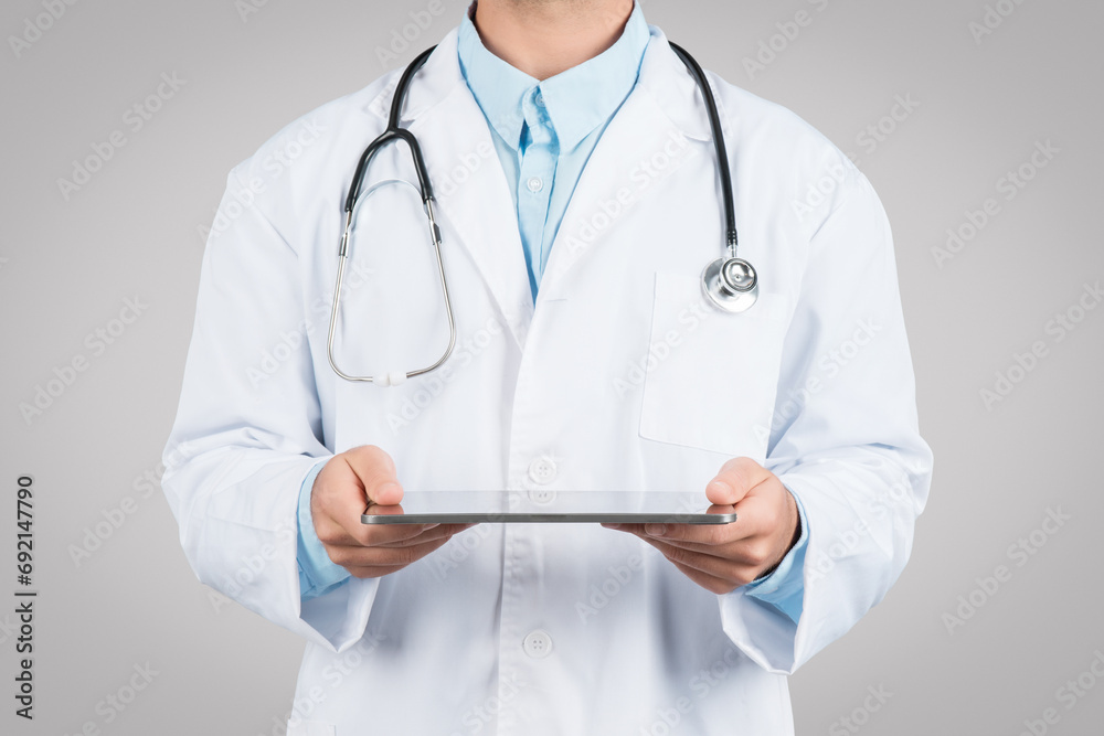 Medicine and technologies. Unrecognizable male doctor using digital tablet, standing on grey studio background Medicine and technologies. Unrecognizable male doctor using digital tablet, standing on grey studio background
