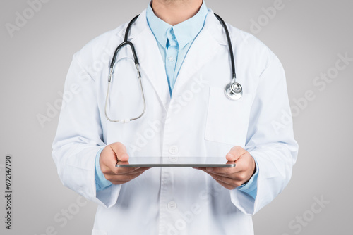 Medicine and technologies. Unrecognizable male doctor using digital tablet, standing on grey studio background