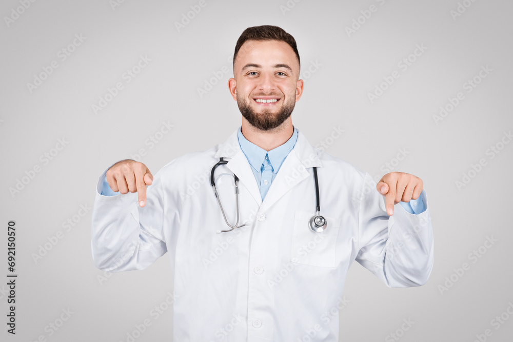 Smiling male doctor pointing down with both hands Smiling male doctor pointing down with both hands