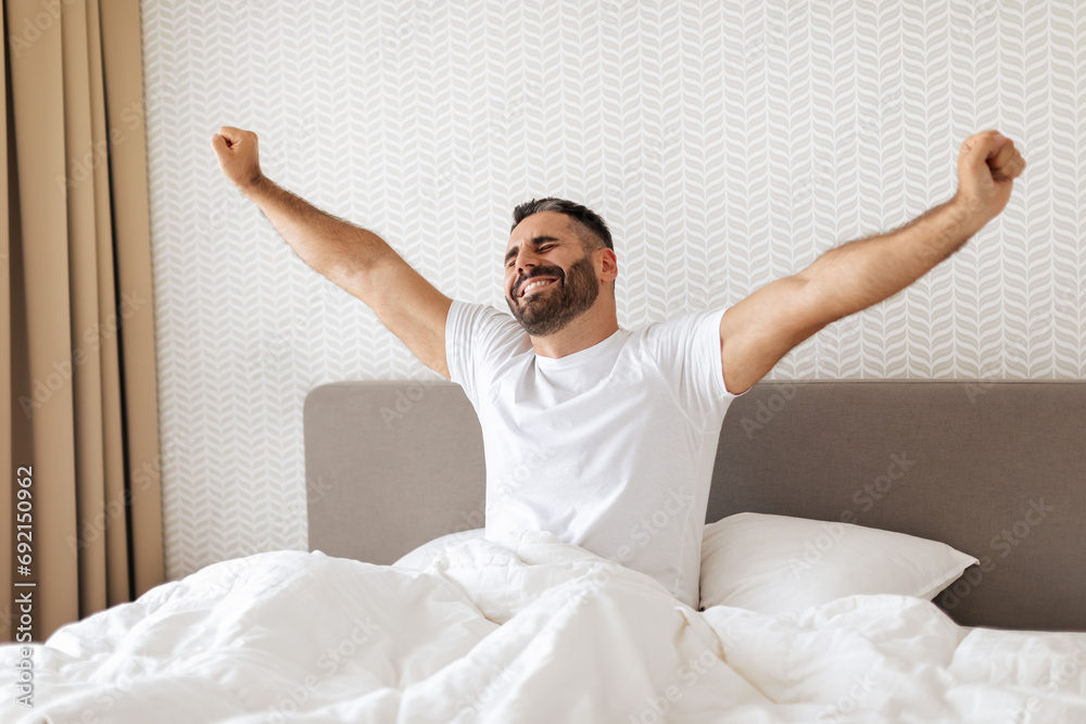 European guy waking up in modern bedroom and stretches arms European guy waking up in modern bedroom and stretches arms