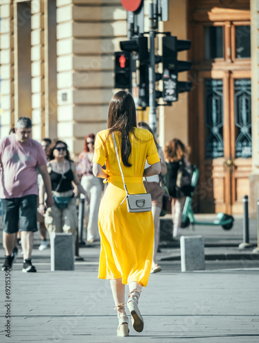 Rear view with a young woman in a elegant yellow dress walking on Victory Street (Calea Victoriei) in the center of Bucharest, Romania. photo