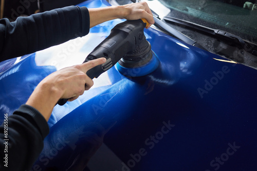 Man with an orbital polisher in car workshop polishing car closeup photo