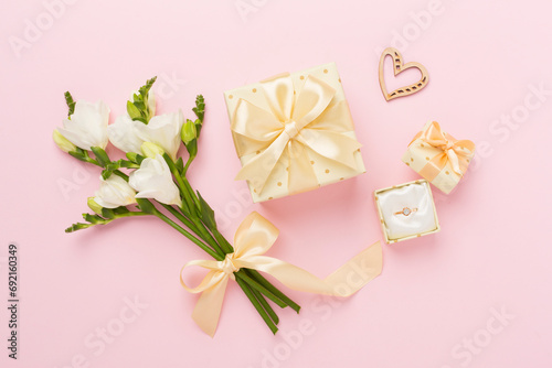 White fresia flower and gift box with diamond ring on color background, top view