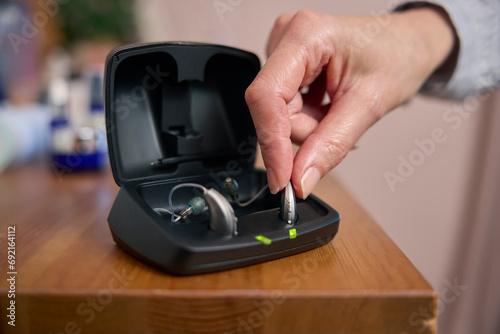 Close Up Of Person Picking Up Wireless Hearing Aid Or Device From Charging Case At Home photo