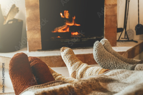 Family resting feet by fireplace on fall or winter time. People warming feet with blanket and socks by cozy fire. photo