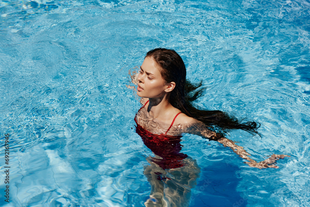 Happy woman swimming in the pool in red swimsuit with loose long hair in the sunshine, skin protection with sunscreen, concept of relaxing on vacation.