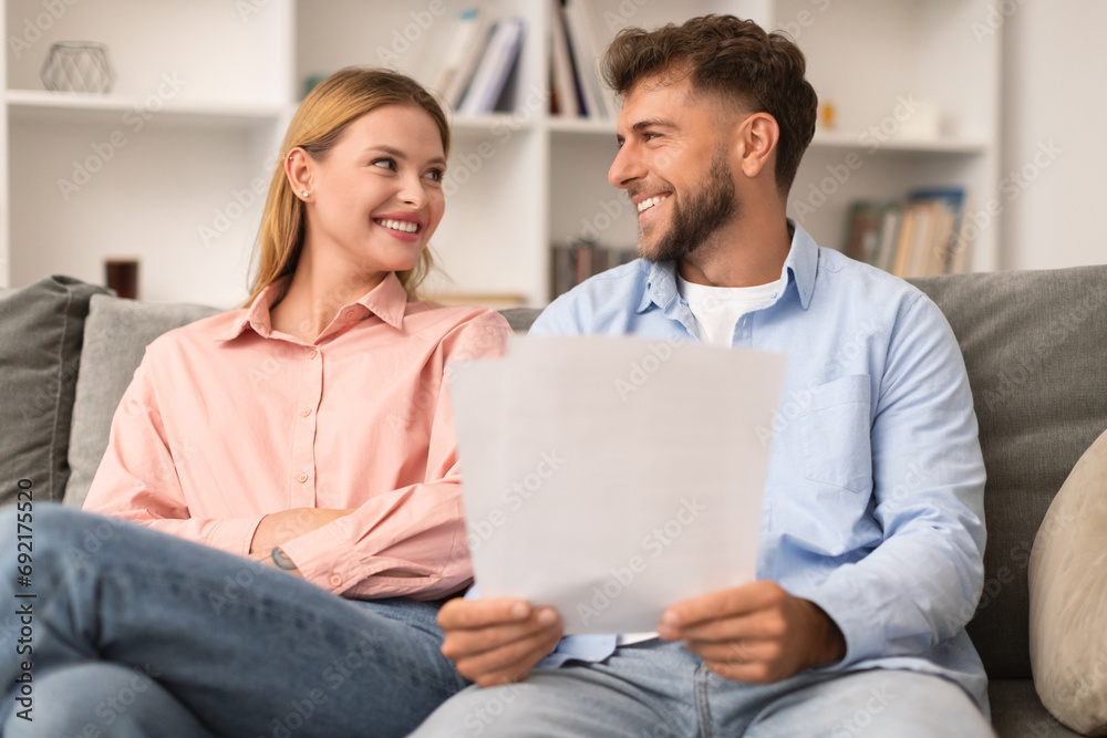 Happy young european spouses checking documents at home