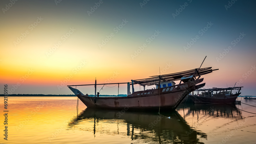 Golden hues paint the tranquil Dammam seaside as boats rest against the morning glow, a serene embrace of nature's beauty in Saudi Arabia.