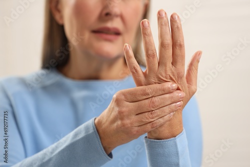 Mature woman suffering from pain in hand against light grey background, closeup. Rheumatism symptom