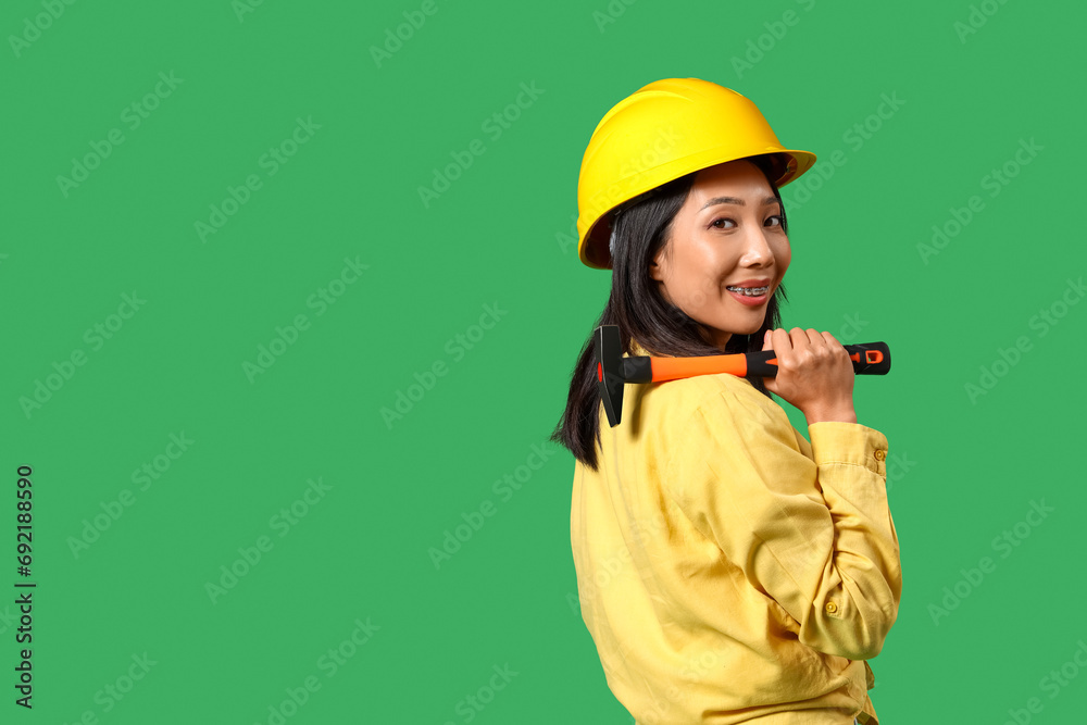 Young Asian woman with hammer on green background Young Asian woman with hammer on green background