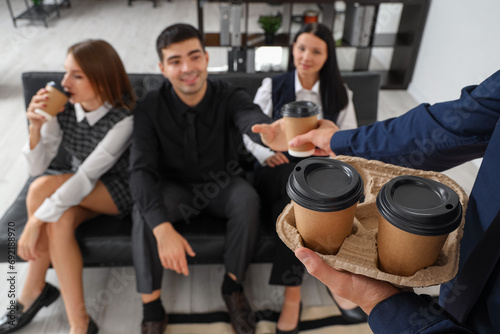 Young man giving coffee to his colleagues in office, closeup photo
