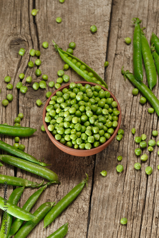 Green peas in closed and open pods, peeled peas in a bowl, scattered pea seeds on a wooden background, top view