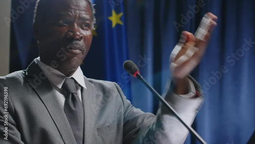 African American senator speaking in mic and gesturing with hand while making public announcement on press conference, EU and US flags in backgroundAfrican American senator speaking in mic and gesturi photo