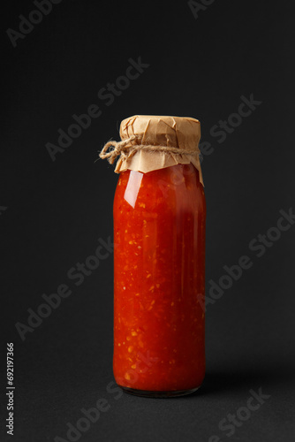 Hot sauce made from chili peppers, paprika, tomatoes and garlic in a jar on a black background.