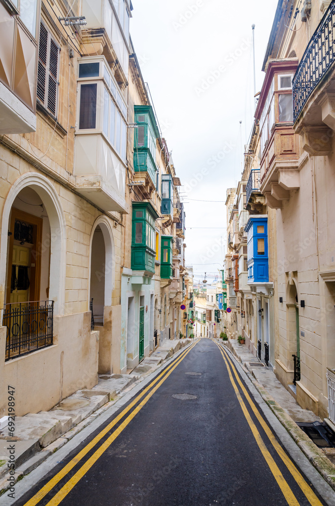 Old medieval street with yellow buildings, beautiful balconies and flower pots in Birgu, Valletta, Malta with nobody