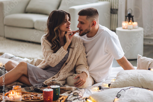 Concept of lazy weekend in bed or romantic home holiday celebration: christmas, new year, saint Valentine's Day. Beautiful young loving couple enjoy time together, embracing, kissing, having fun photo