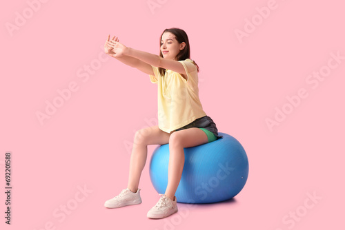 Sporty young woman training on fitball on pink background