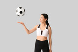 Sporty young Asian woman with soccer ball on light background