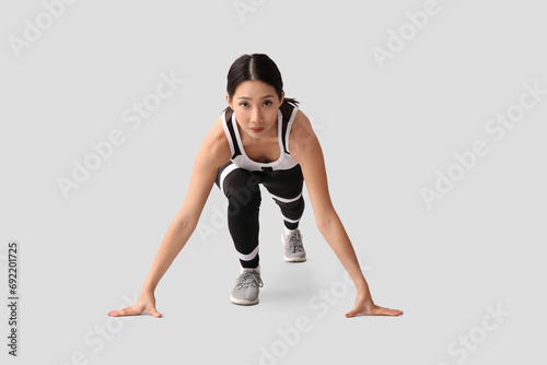 Sporty young Asian woman getting ready to run on light background