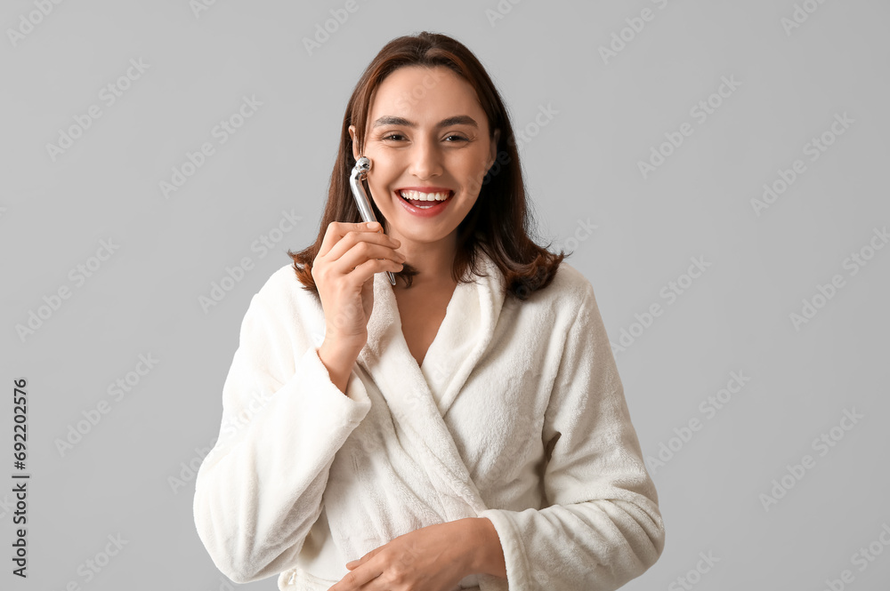 Young woman in bathrobe massaging face on light background Young woman in bathrobe massaging face on light background