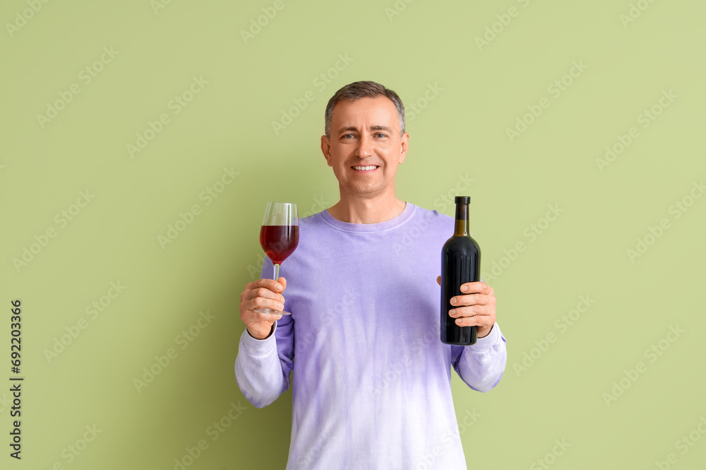 Mature man with glass and bottle of red wine on green background Mature man with glass and bottle of red wine on green background