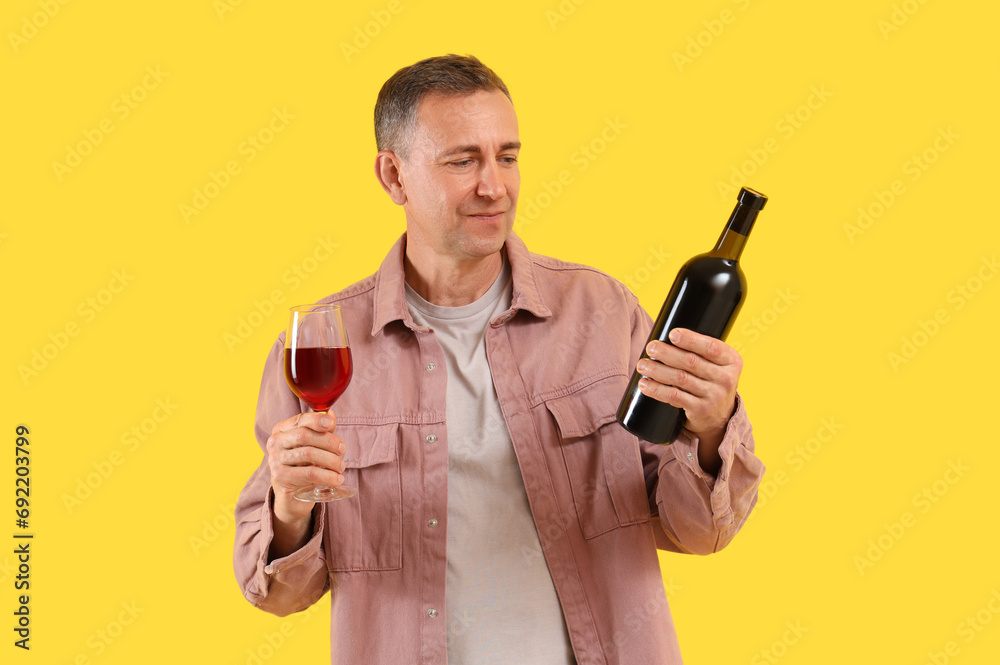 Mature man with glass and bottle of red wine on yellow background Mature man with glass and bottle of red wine on yellow background