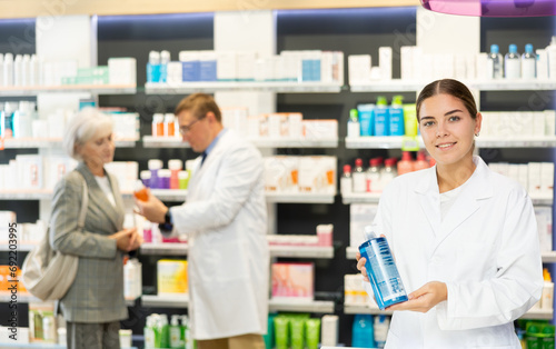 Young female pharmacist in medical uniform posing with product intimate hygiene in her hands in pharmacy