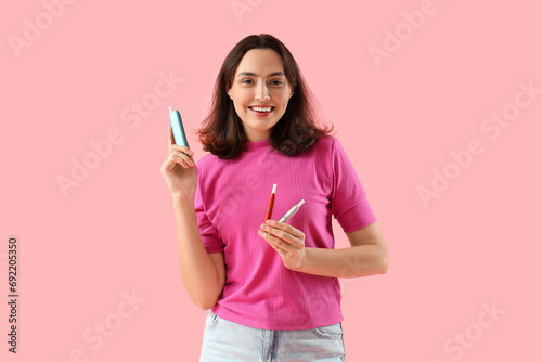 Young woman with electronic cigars on pink background