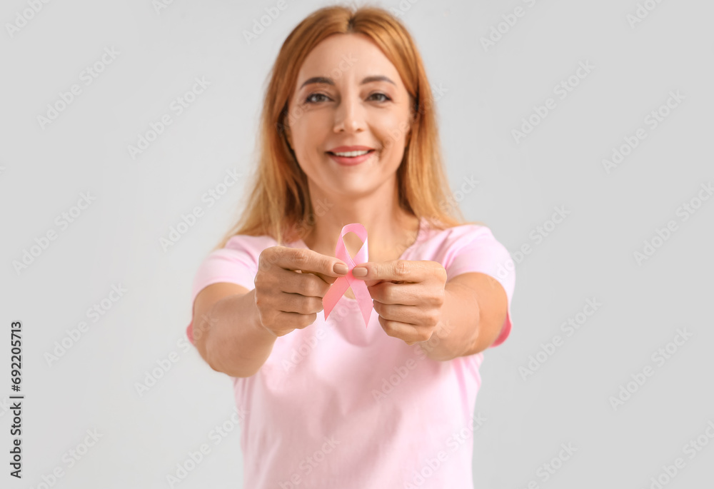 Mature woman with pink ribbon on light background, closeup. Breast cancer awareness concept Mature woman with pink ribbon on light background, closeup. Breast cancer awareness concept