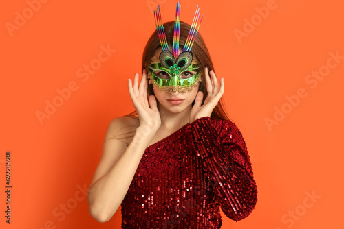 Beautiful young woman in carnival mask on orange background photo