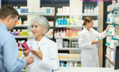 Male customer consulting with elderly female pharmacist at pharmacy