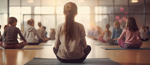 Back view of PE teacher leading Yoga class and meditating with elementary students at school gym. Copy space image. Place for adding text or design photo