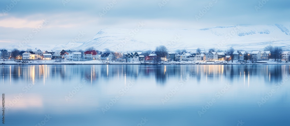 Fototapeta premium Beautiful houses reflected in lake Tjornin in Reykjavik Iceland during the blue hour in winter. Copy space image. Place for adding text or design