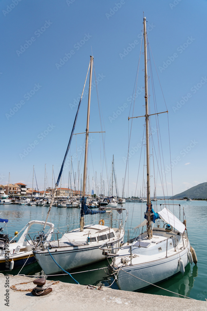 Sailing boats docked at a peaceful marina, their masts pointing towards a clear blue sky, in a tranquil seaside setting