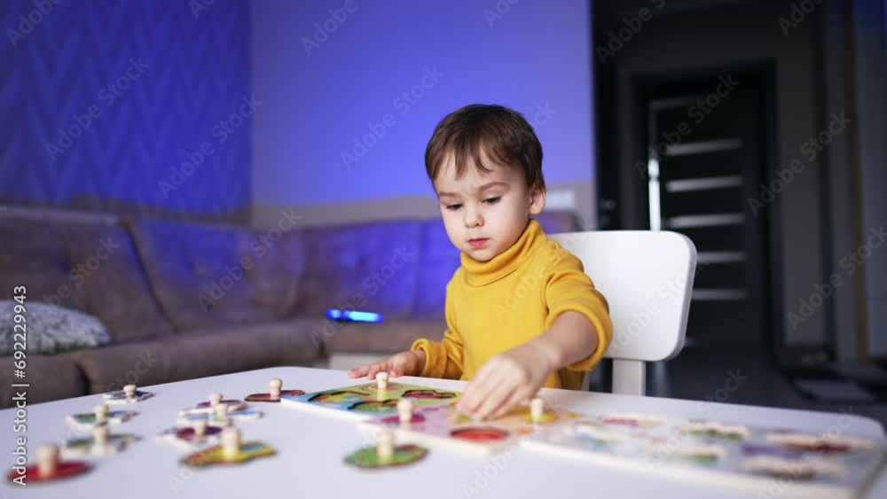Beautiful dark-haired baby boy in yellow sweater sitting at desk. Smart little kid collecting puzzles. Beautiful dark-haired baby boy in yellow sweater sitting at desk. Smart little kid collecting puzzles.