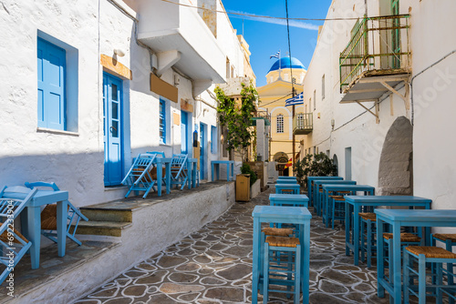 Tavern chairs and tables on narrow street with typical Greek style architecture in Kimolos village, Kimolos island, Cyclades, Greece