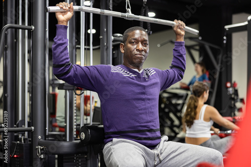 African man doing exercises on lat pull down machine in gym